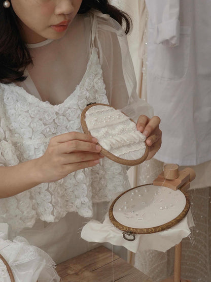 Person holding a lace doily over a wooden embroidery hoop