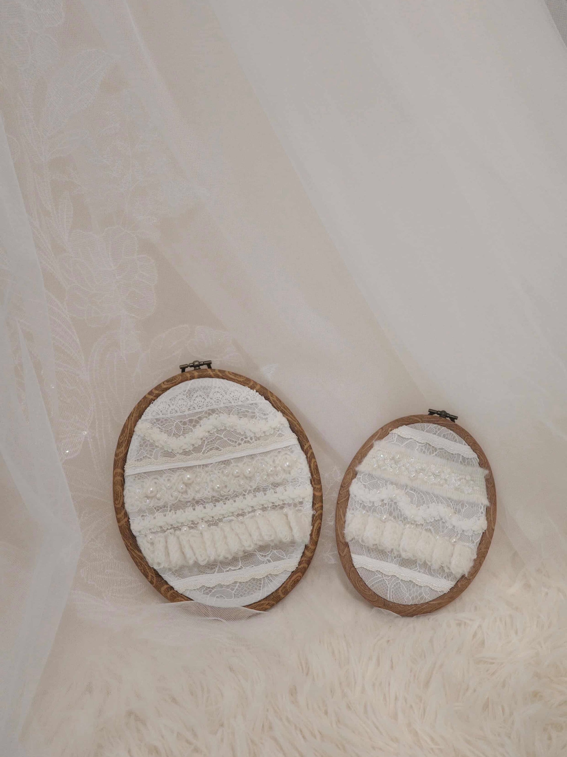 Two round embroidered pieces in wooden frames on a textured white background