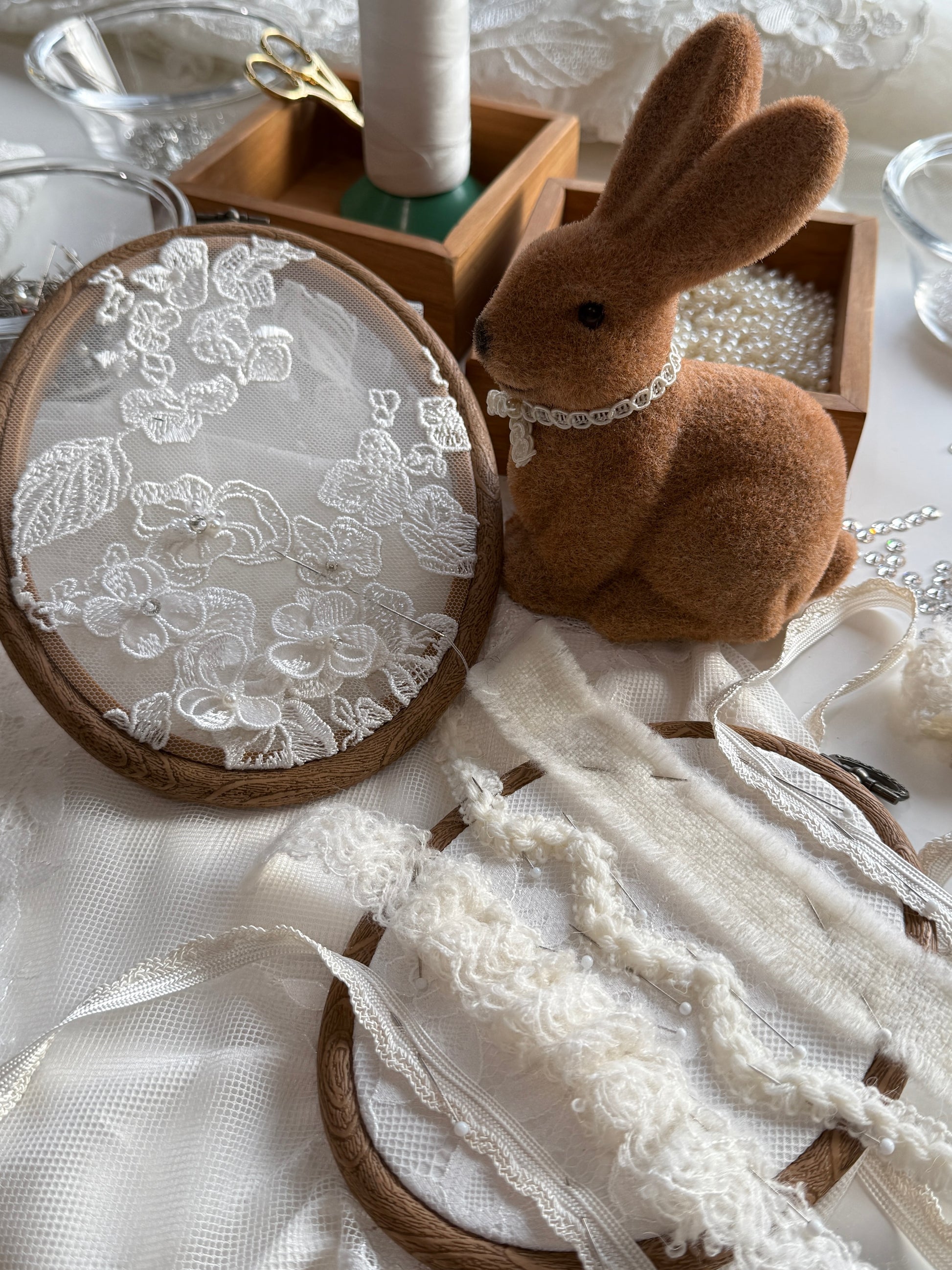 Embroidery hoop with lace and a plush rabbit toy on a white fabric background