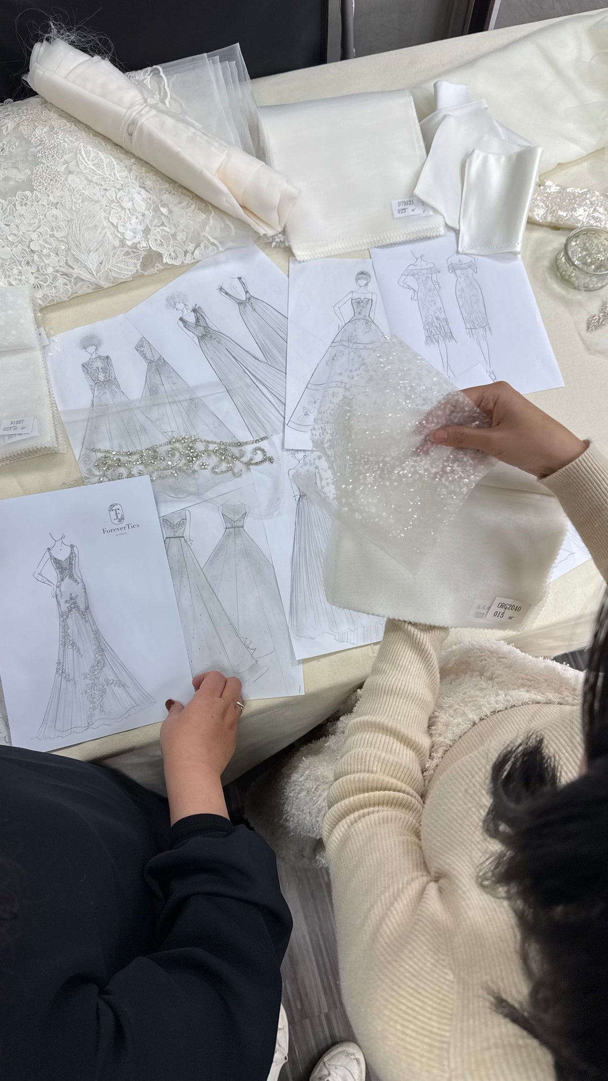 Bridal designers reviewing wedding dress sketches, lace and fabric swatches while developing a bespoke bridal gown.