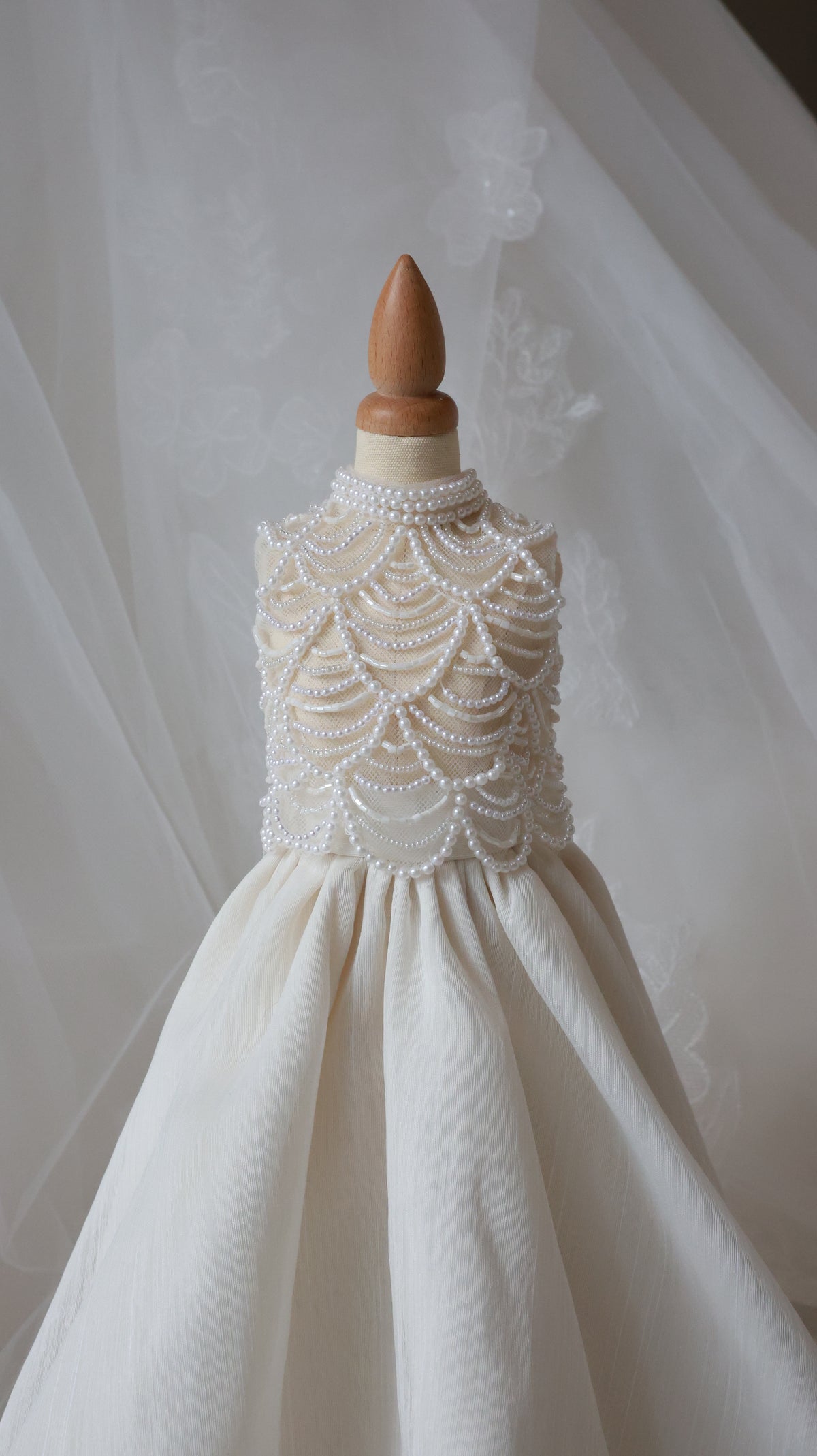 White wedding dress with intricate lace detailing on a wooden hanger against a neutral background