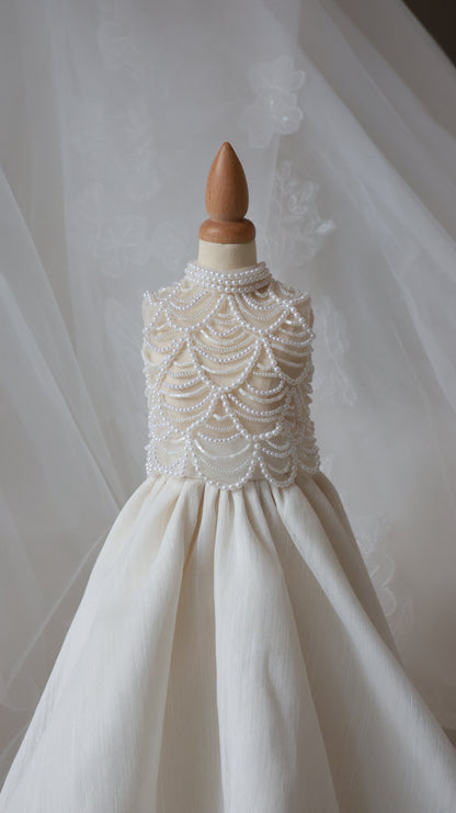 White wedding dress with intricate lace detailing on a wooden hanger against a neutral background